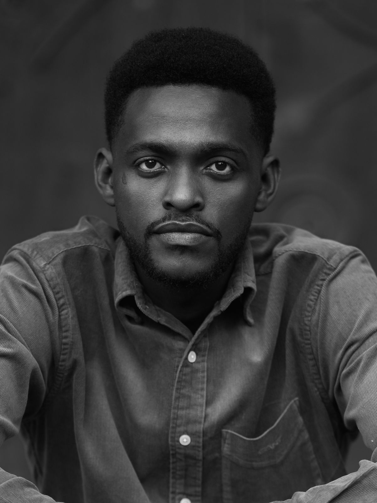 Black-and-white close portrait of a man in a denim shirt looking directly at the camera