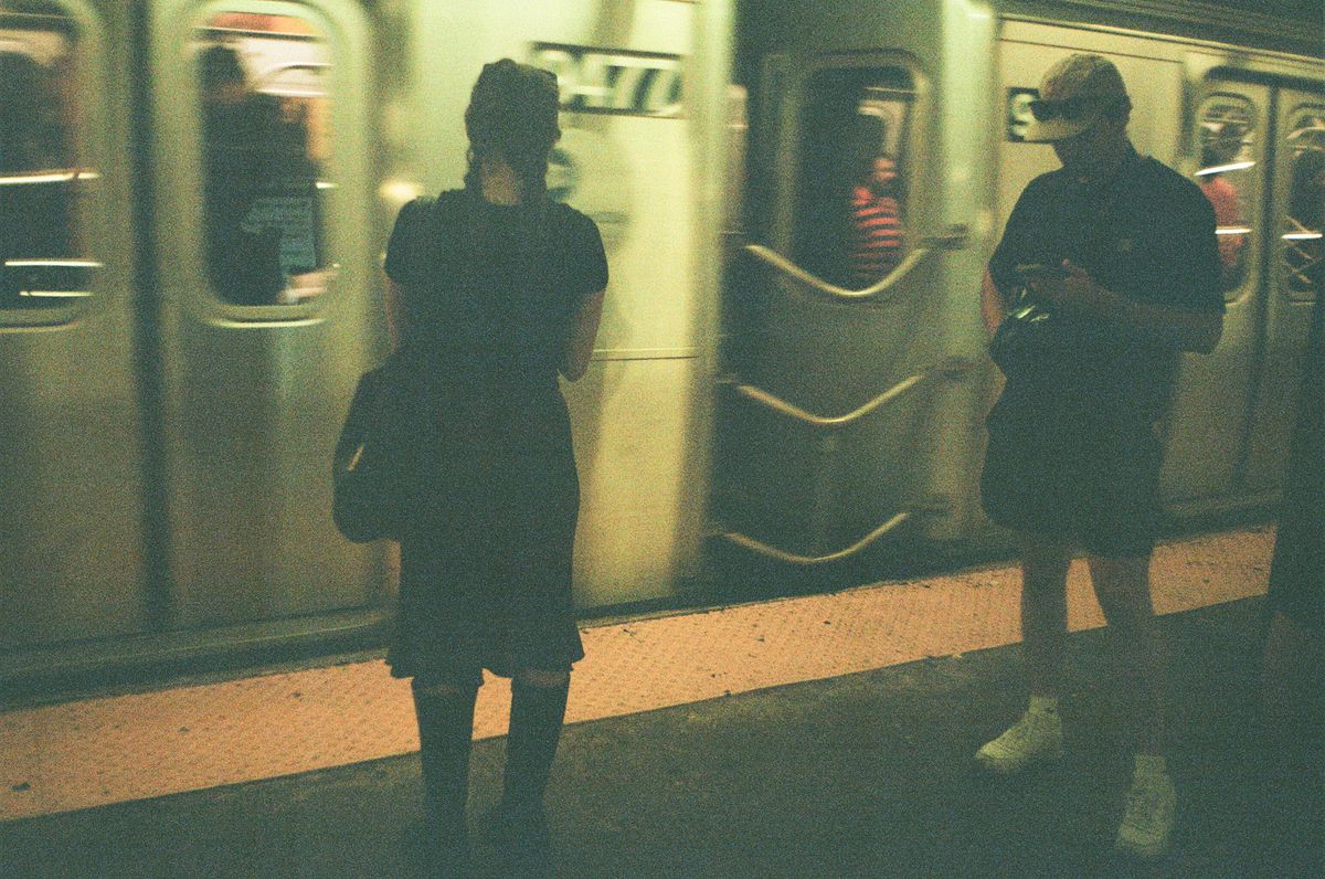 Two commuters in silhouette waiting as a subway train pulls into a dimly lit station