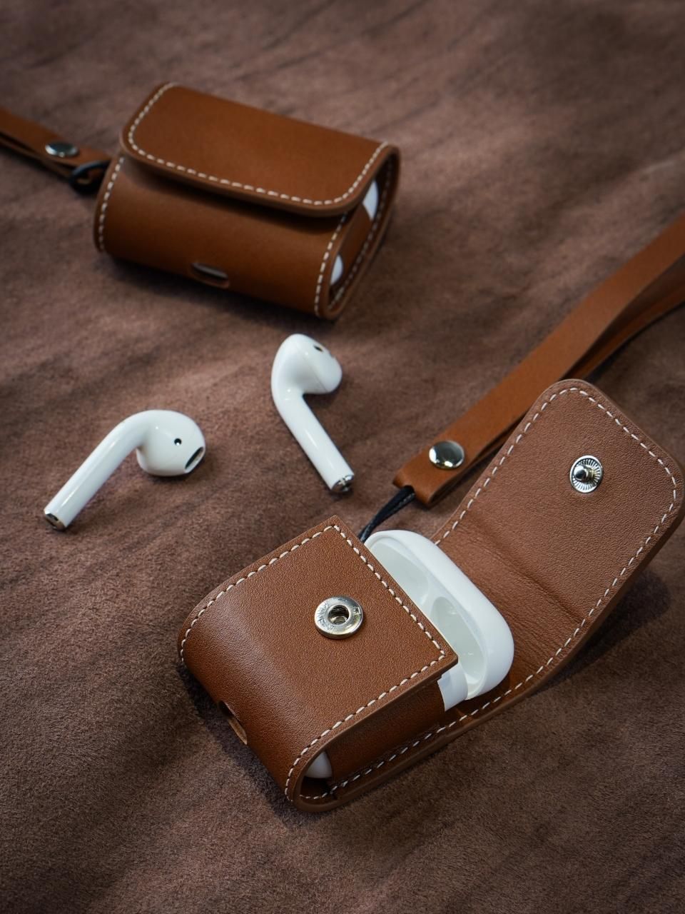 Leather AirPods case, open, with both earbuds resting on a leather backdrop