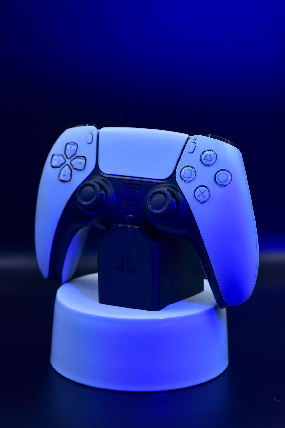 Modern wireless game controller displayed on a stand, lit by cool blue studio lighting against a dark background