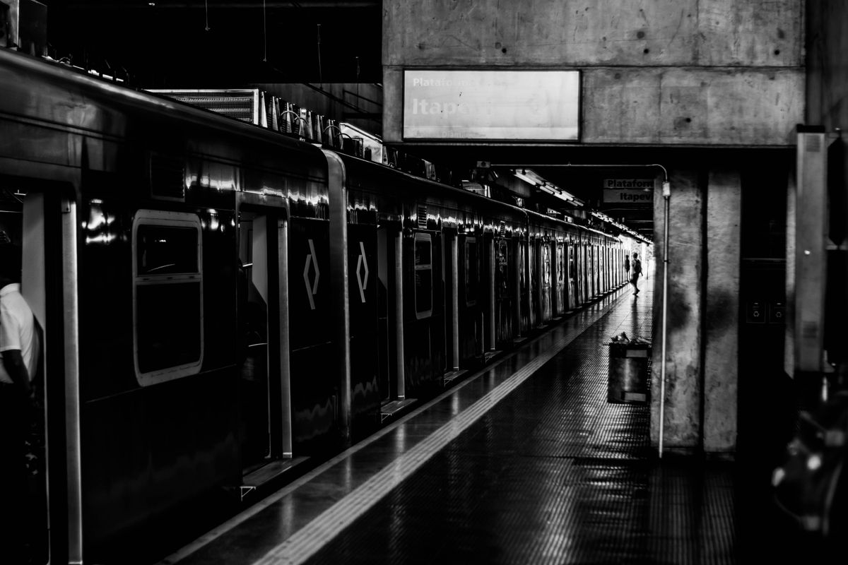 Black-and-white photo of a train pulling into a platform as a lone commuter waits in the distance