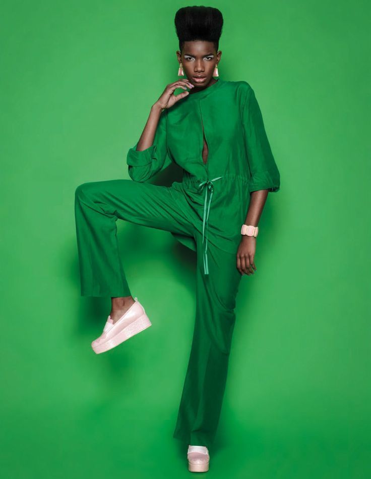 Portrait in a green jumpsuit against a matching green backdrop, one leg raised