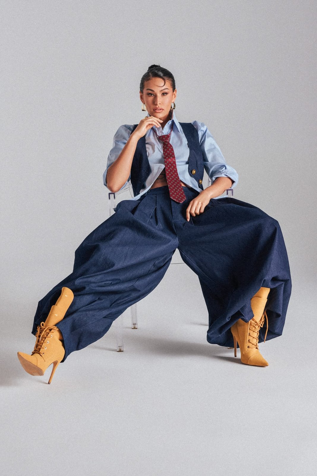 Studio portrait in a cropped vest, tie, and voluminous wide-leg trousers with tan lace-up boots