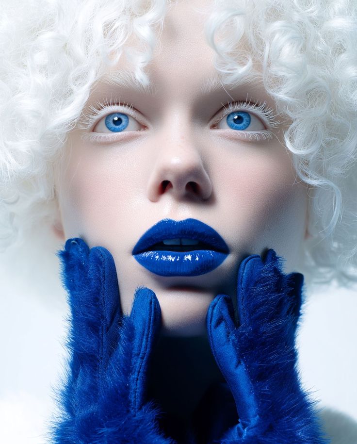 Beauty portrait with white curls, cobalt lips and blue fur gloves framing the face