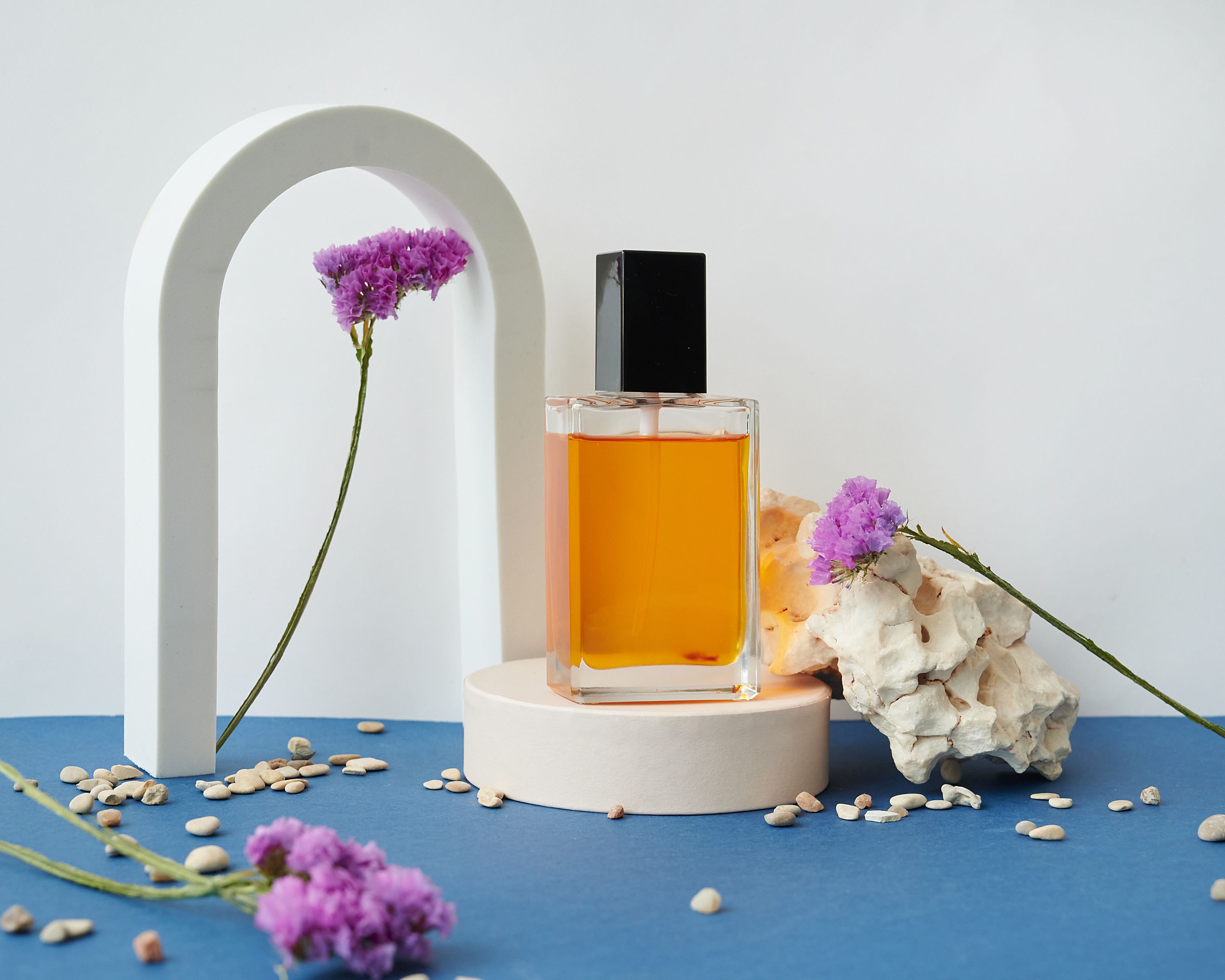 Amber perfume bottle staged with dried flowers between a plaster arch and stone
