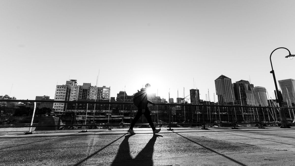 Silhouette of a person walking along a waterfront promenade at sunrise with a city skyline behind