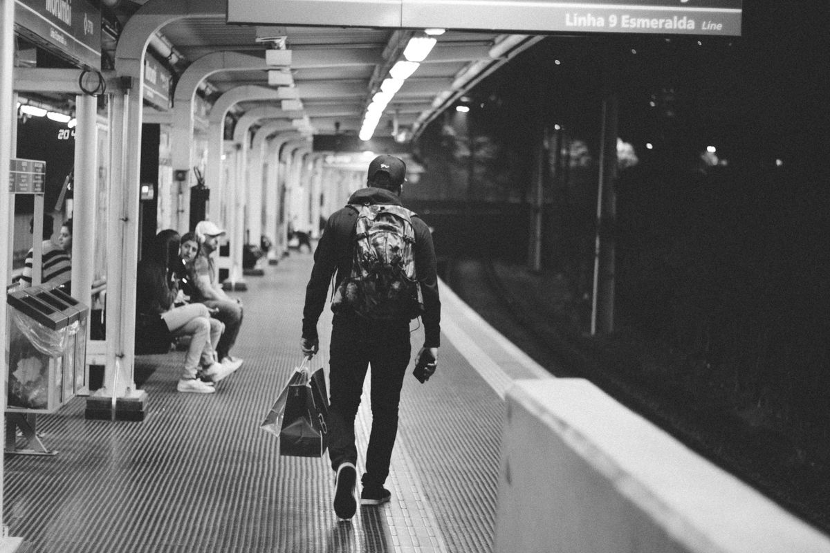 Black-and-white photo of a commuter walking away down a subway platform, carrying bags
