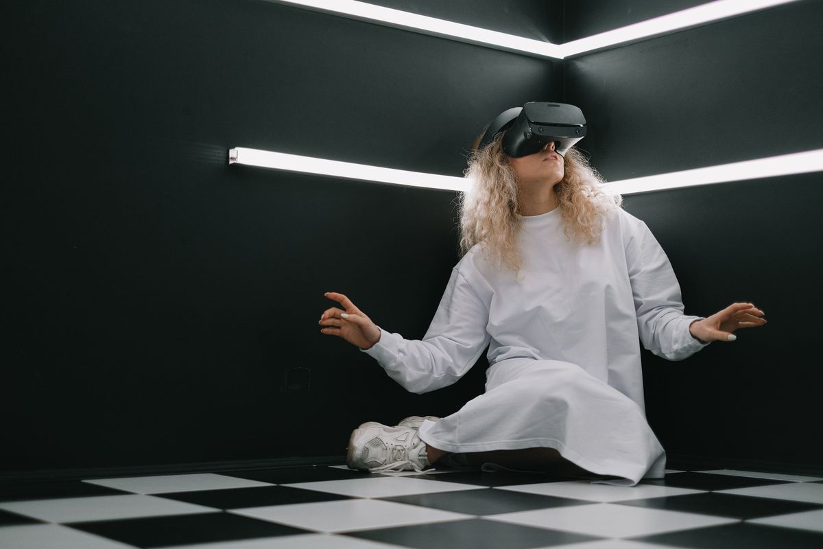 Person wearing a black VR headset, kneeling in a minimalist dark room lit by white LED strip lighting